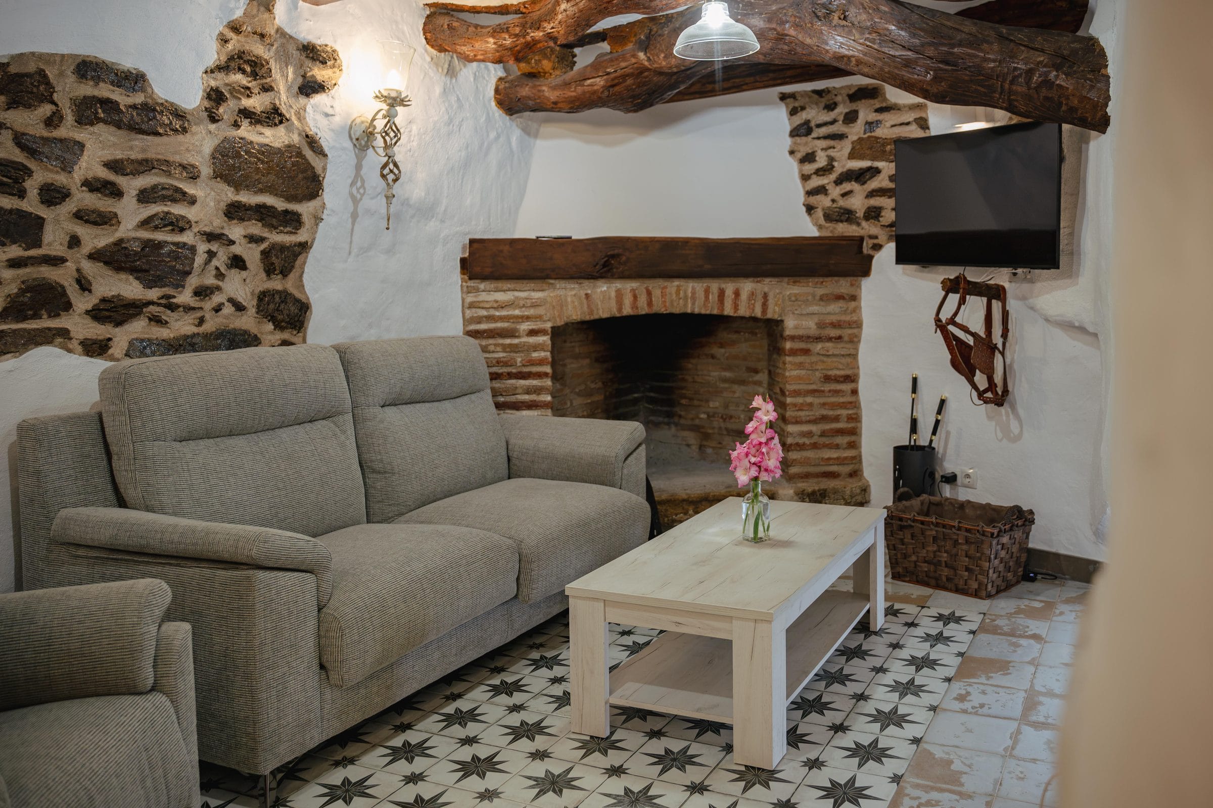 Salón con chimenea de ladrillo, sofá y vigas de madera, en Casa Cuadra, en Albondón